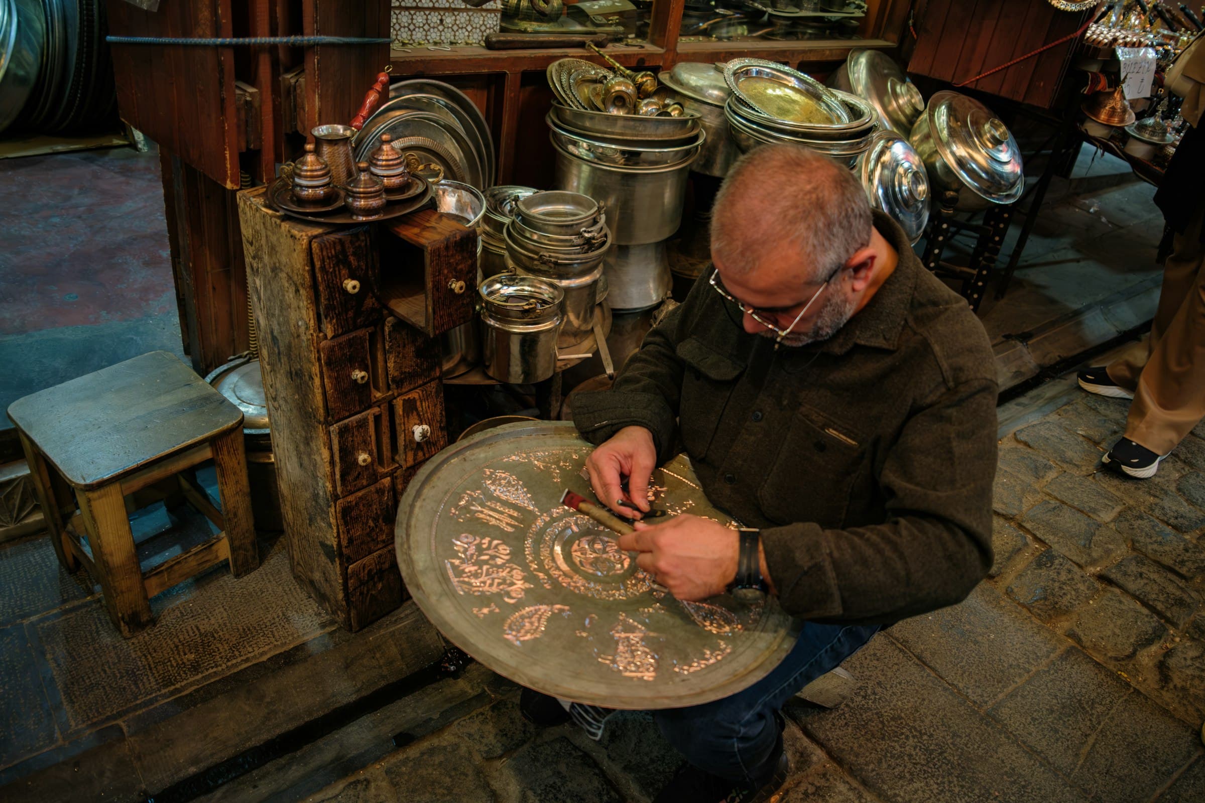 An artisan engraving a decorative metal tray at the bench