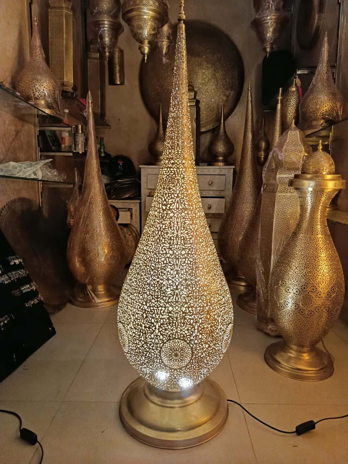Tall hand-pierced brass teardrop floor lamp, lit, in the workshop
